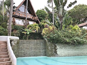 Un resort tropical con piscina, terraza de madera y exuberante vegetación.
