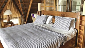 A bed with striped bedding in a room with wooden beams and a sloped ceiling. - Waimea Luxury Houses - Adults Only (Puerto Galera)