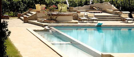 A swimming pool with a sun terrace, lounge chairs, and a small garden area.