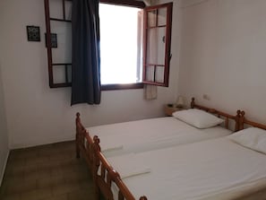 Et soveværelse med to enkeltsenge, en træsenggavl, et natbord med lampe og et vindue med gardiner.