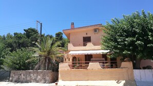 Una casa de dos pisos con un balcón, rodeada de follaje y un cielo despejado.