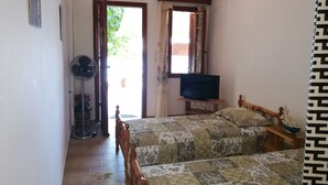Un dormitorio con dos camas, un televisor sobre un mueble, un ventilador y una ventana con cortinas.