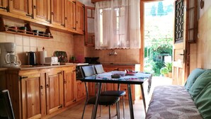 Una cocina con armarios de madera, una mesa de comedor con sillas y vista al jardín a través de una puerta abierta.