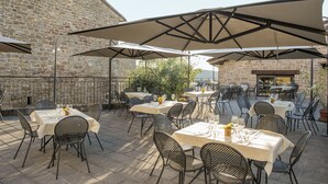 An outdoor patio with tables and chairs, covered by large umbrellas, set against a stone wall. - Albergo Il Rientro (Cannara)