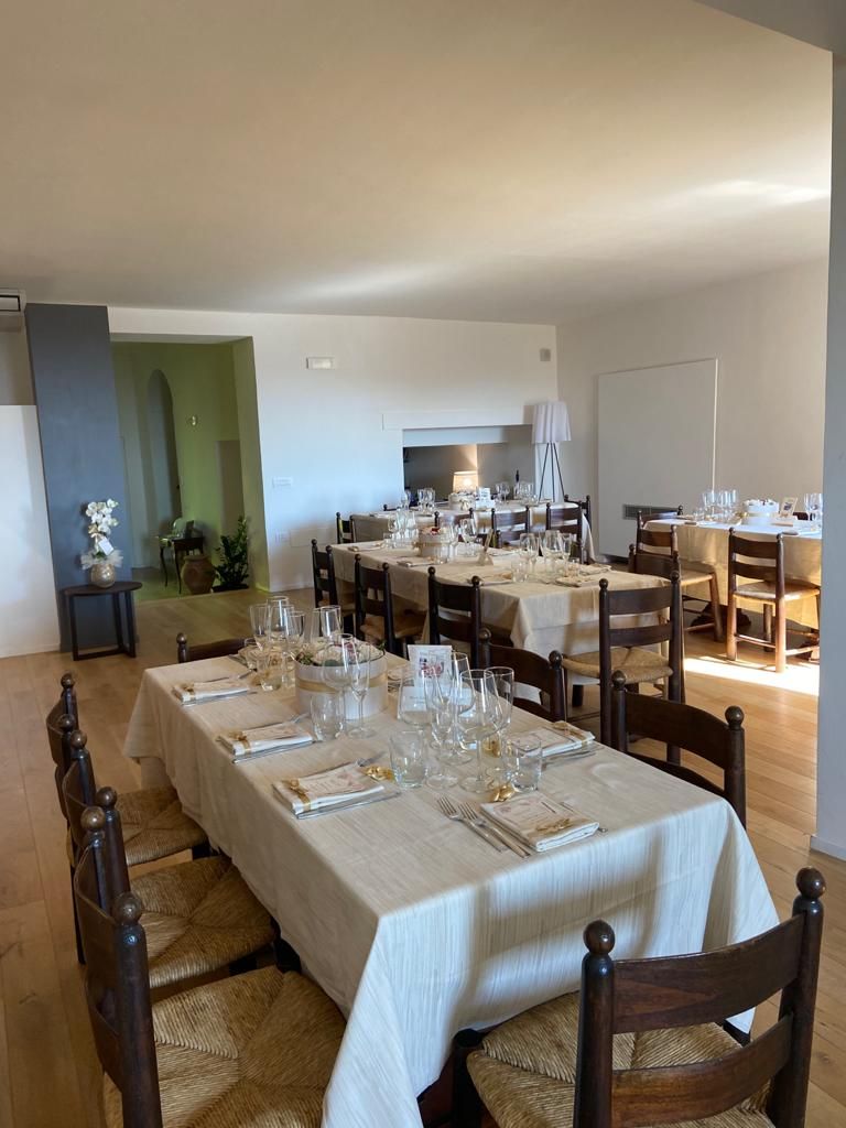 Comedor con varias mesas dispuestas para una comida, sillas y una escalera que sube a un nivel superior.