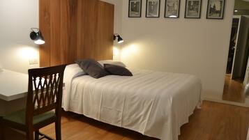 Een slaapkamer met een houten hoofdbord, een bed met wit beddengoed, twee bedlampen en vier ingelijste foto's aan de muur.