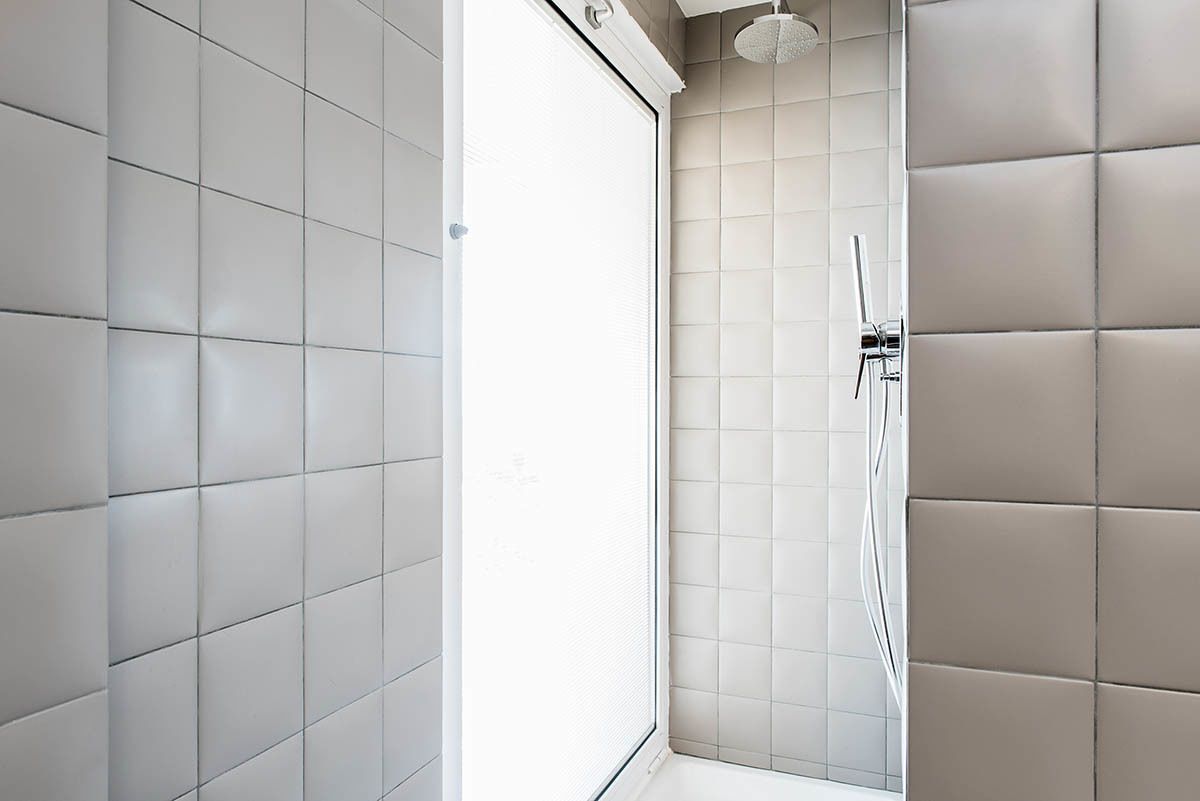 Un baño moderno con zona de ducha, paredes con azulejos y puerta de vidrio.