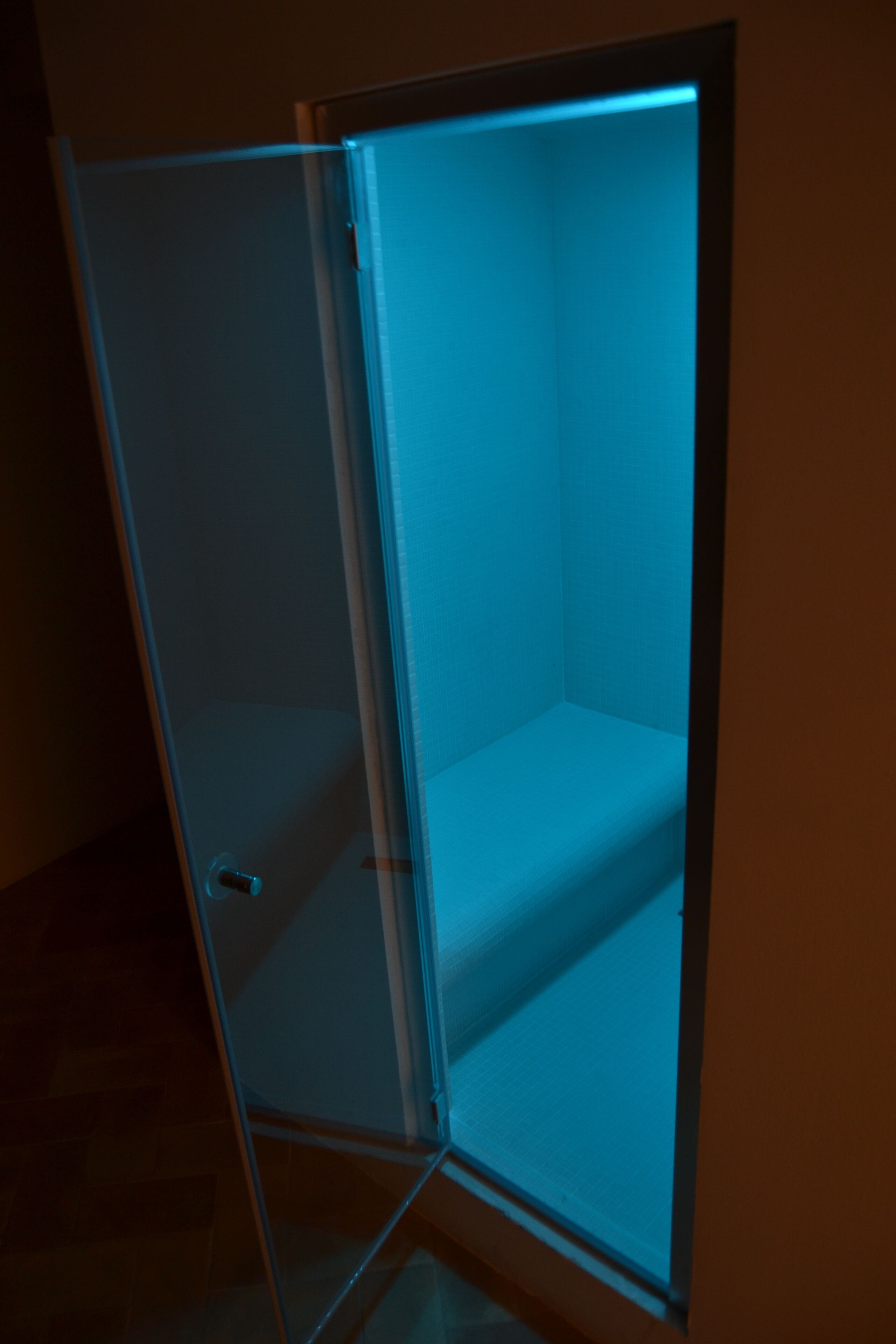A glass-walled room with a blue light, a door, and a visible floor.