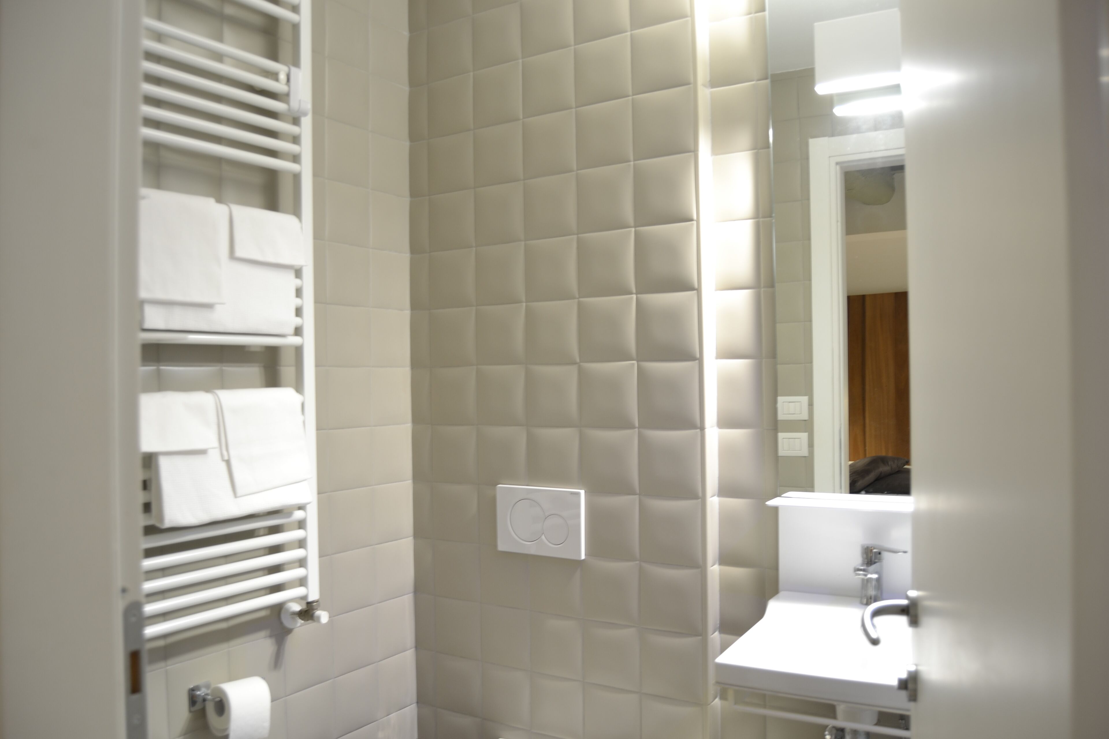 Une salle de bain avec un mur recouvert de carreaux blancs, un porte-serviettes, un support à papier toilette et un miroir.