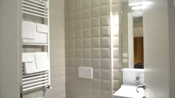 Une salle de bain avec un mur recouvert de carreaux blancs, un porte-serviettes, un support à papier toilette et un miroir.