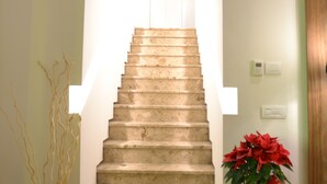 A staircase with a light fixture above, leading to an upper floor. There are two vases with plants on either side of the stairs. - Albergo Il Rientro (Cannara)