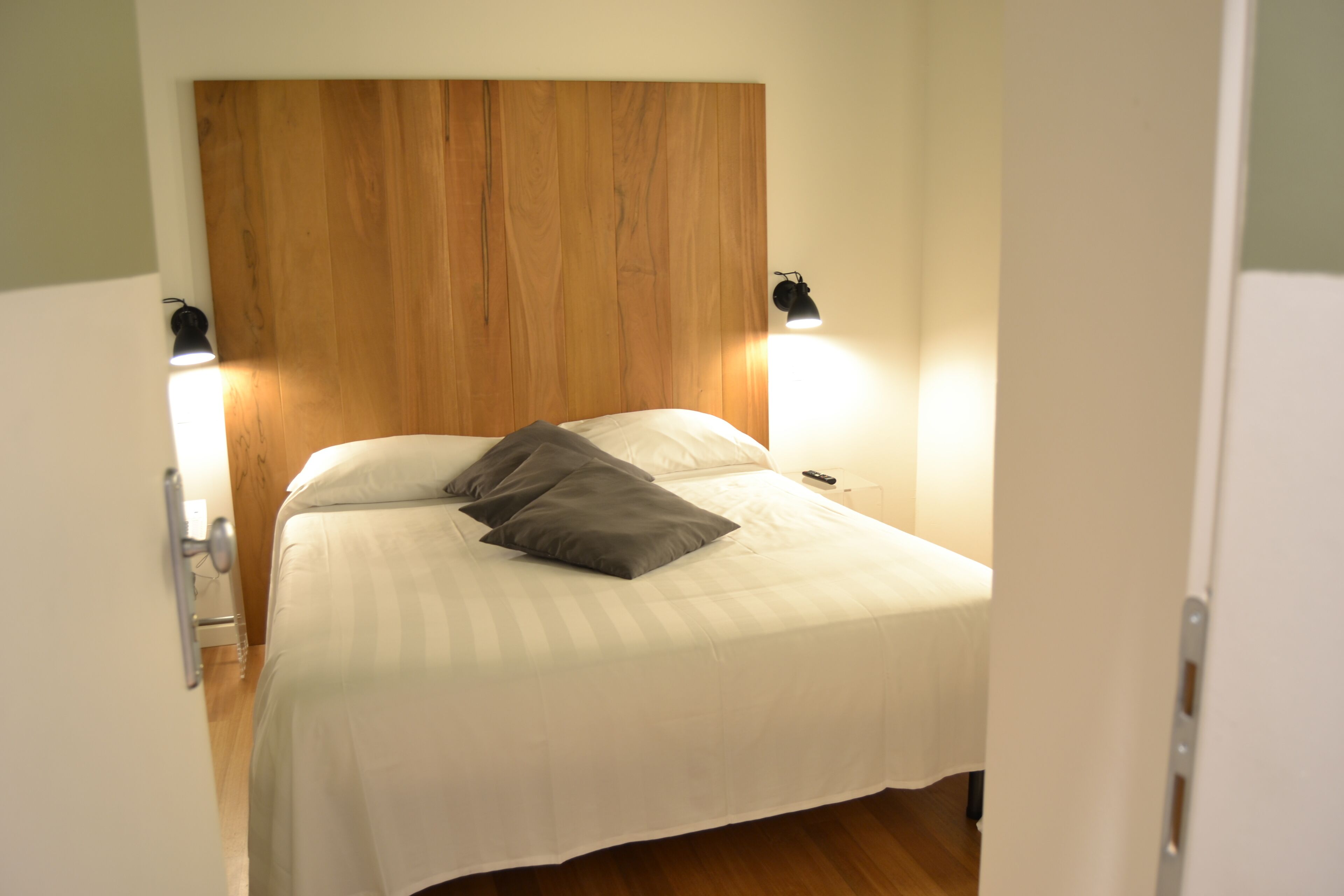 A neatly made bed with a wooden headboard, two bedside lamps, and a single pillow.