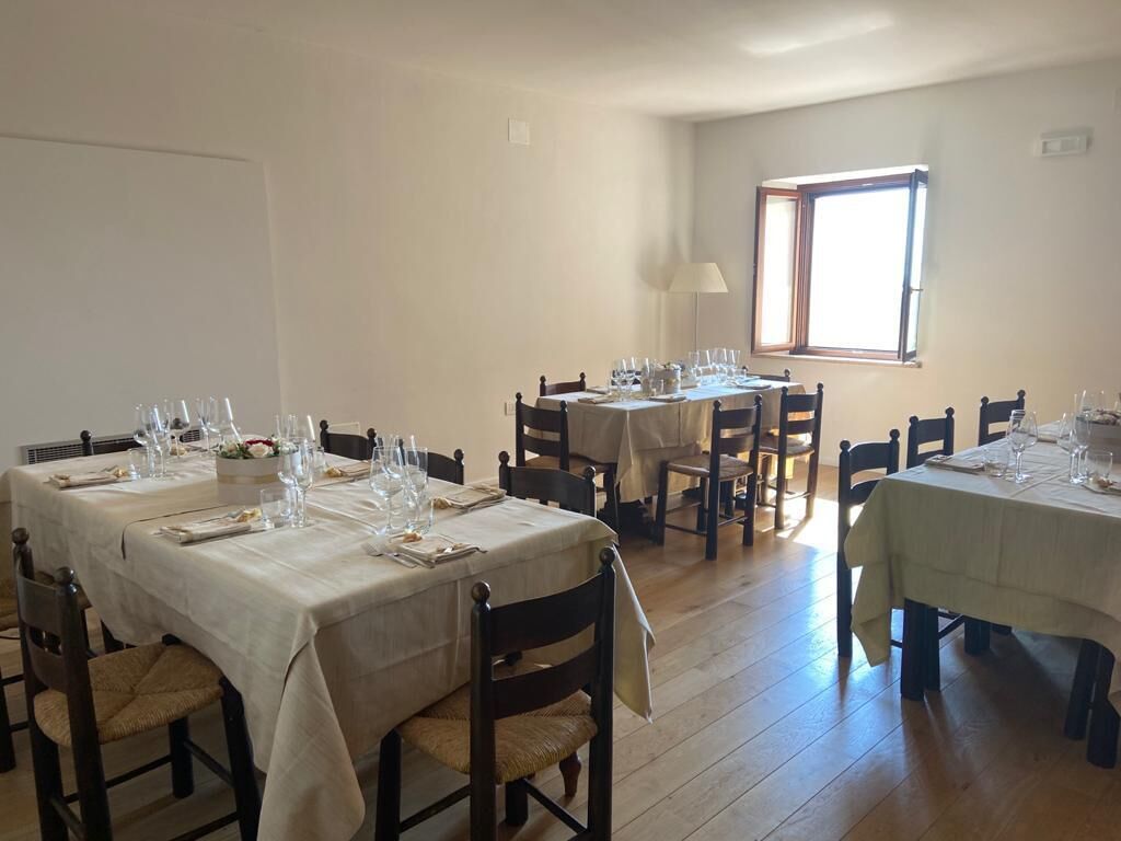 Un espace repas avec plusieurs tables dressées pour le repas, des chaises en bois et une fenêtre laissant entrer la lumière naturelle.