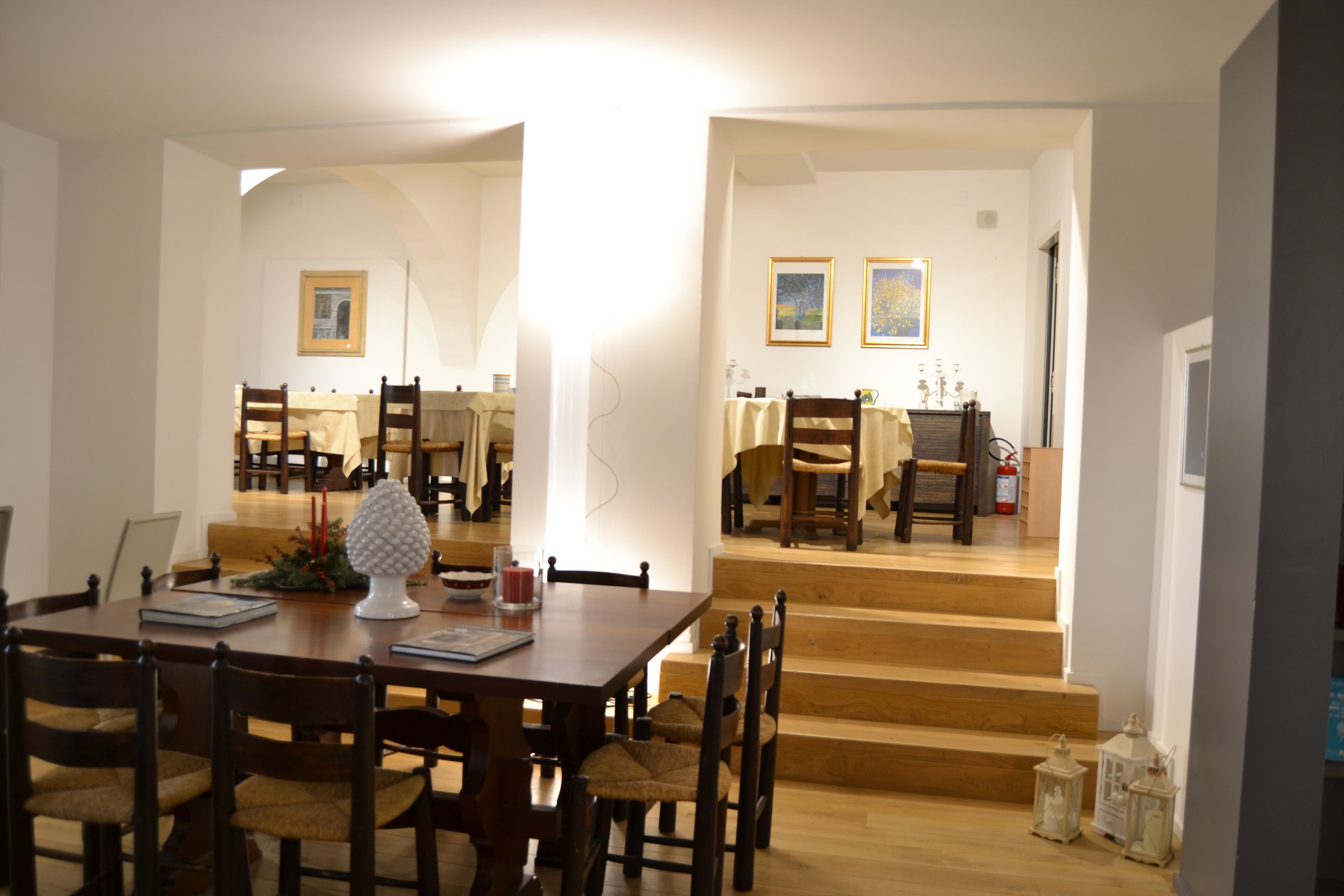 Un comedor con una mesa y sillas de madera, una escalera que lleva a otra habitación y cuadros en la pared.