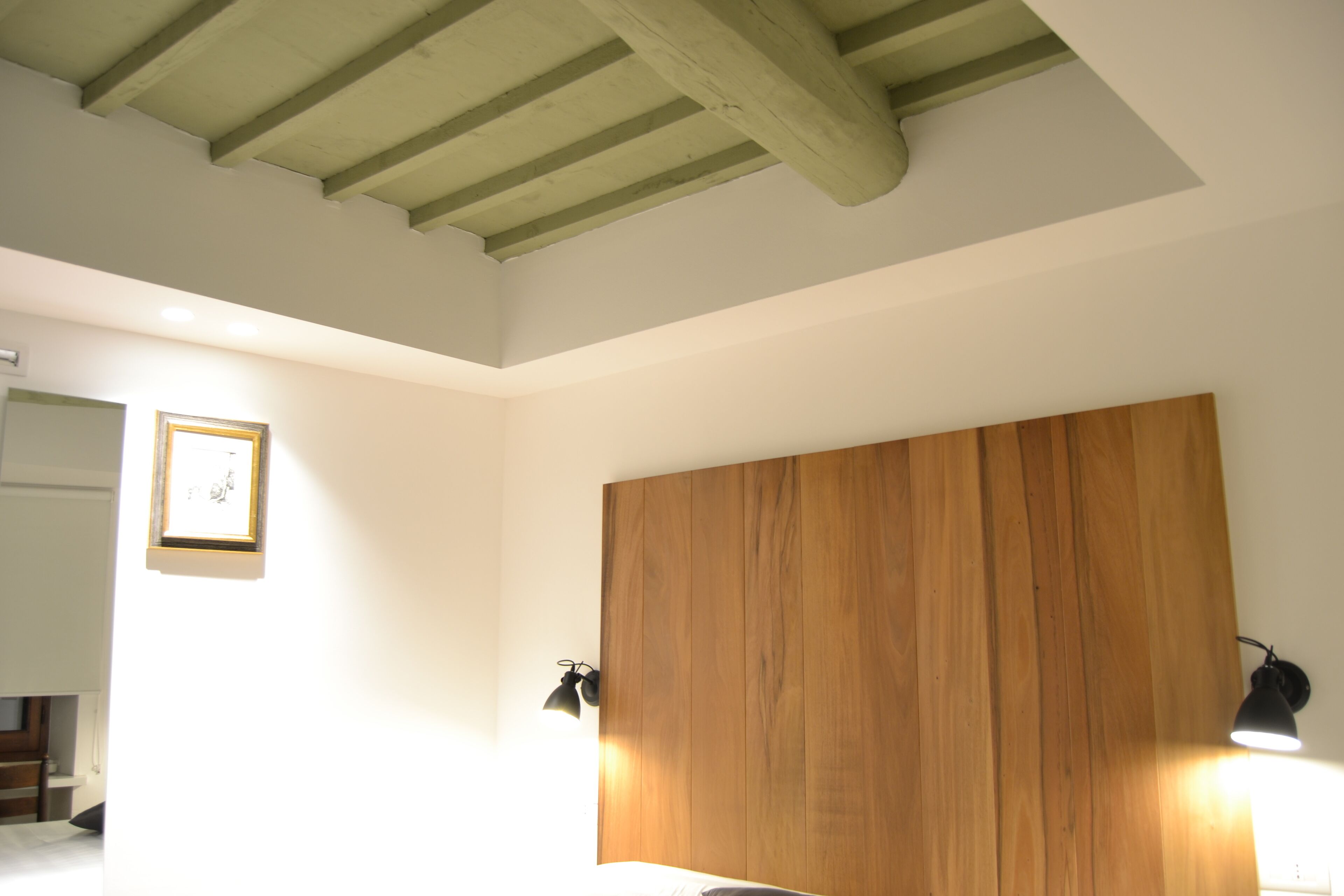 Un dormitorio con cabecera de madera, dos lámparas de noche y un cuadro en la pared.