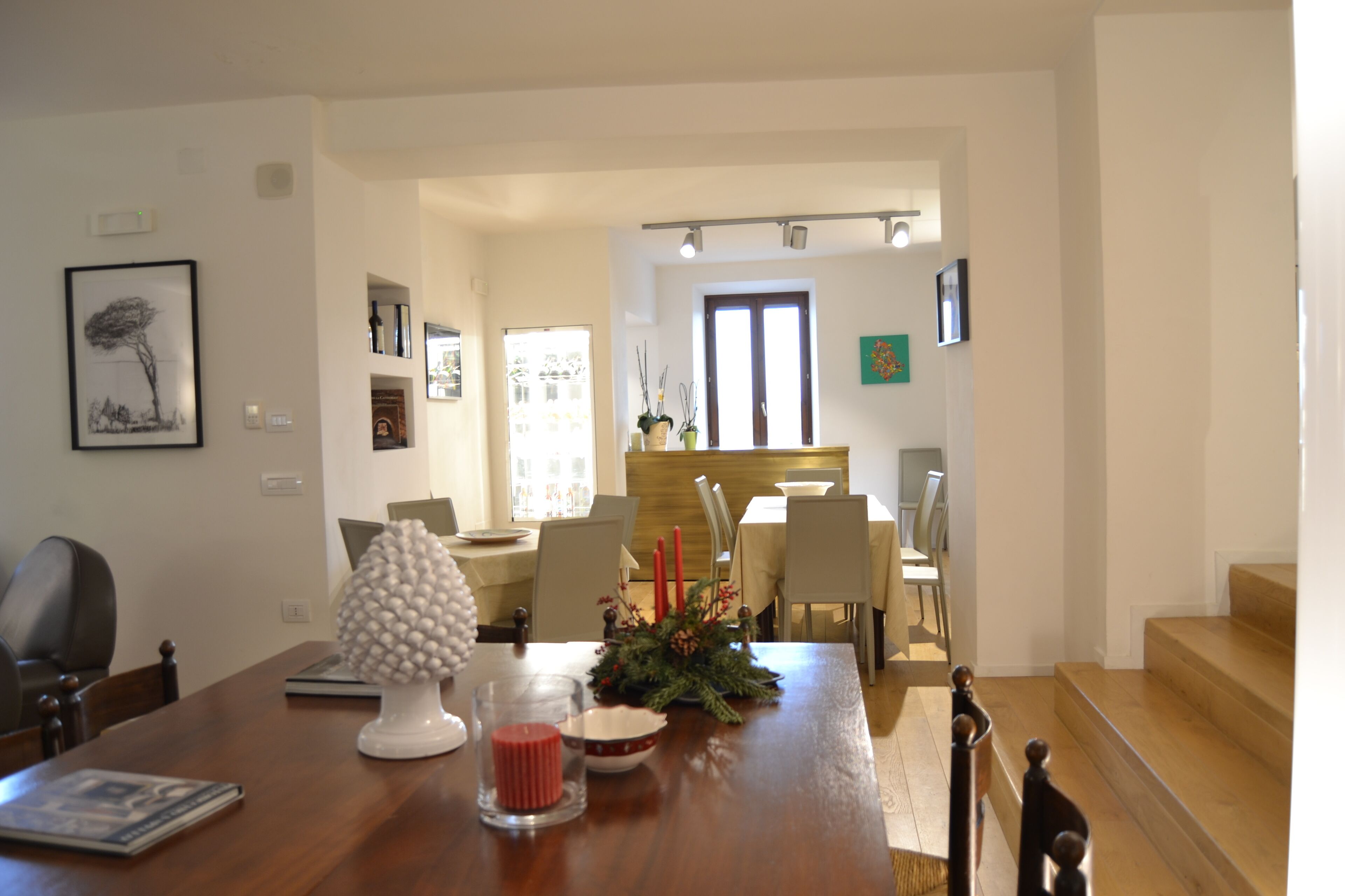 Un coin repas avec une table en bois, des chaises et un vase contenant des bougies rouges. Un tableau encadré est accroché au mur, et il y a une fenêtre avec des rideaux.