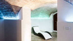 A sunlit room with a stone ceiling, a white wall, and a black and white lounge chair. - Albergo Il Rientro (Cannara)