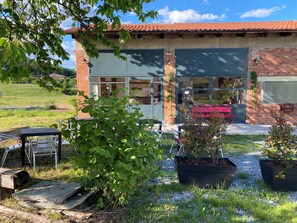 Un edificio con fachada de ladrillo, ventanas grandes y techo rojo. Hay áreas de estar al aire libre con sillas y mesas de metal.