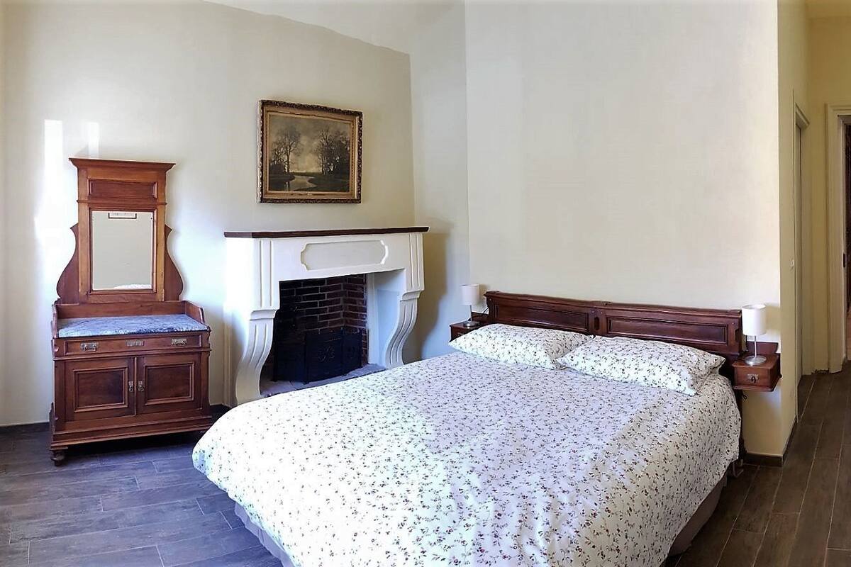 Een slaapkamer met een groot bed, een houten dressoir, een open haard en een deur naar een andere kamer.