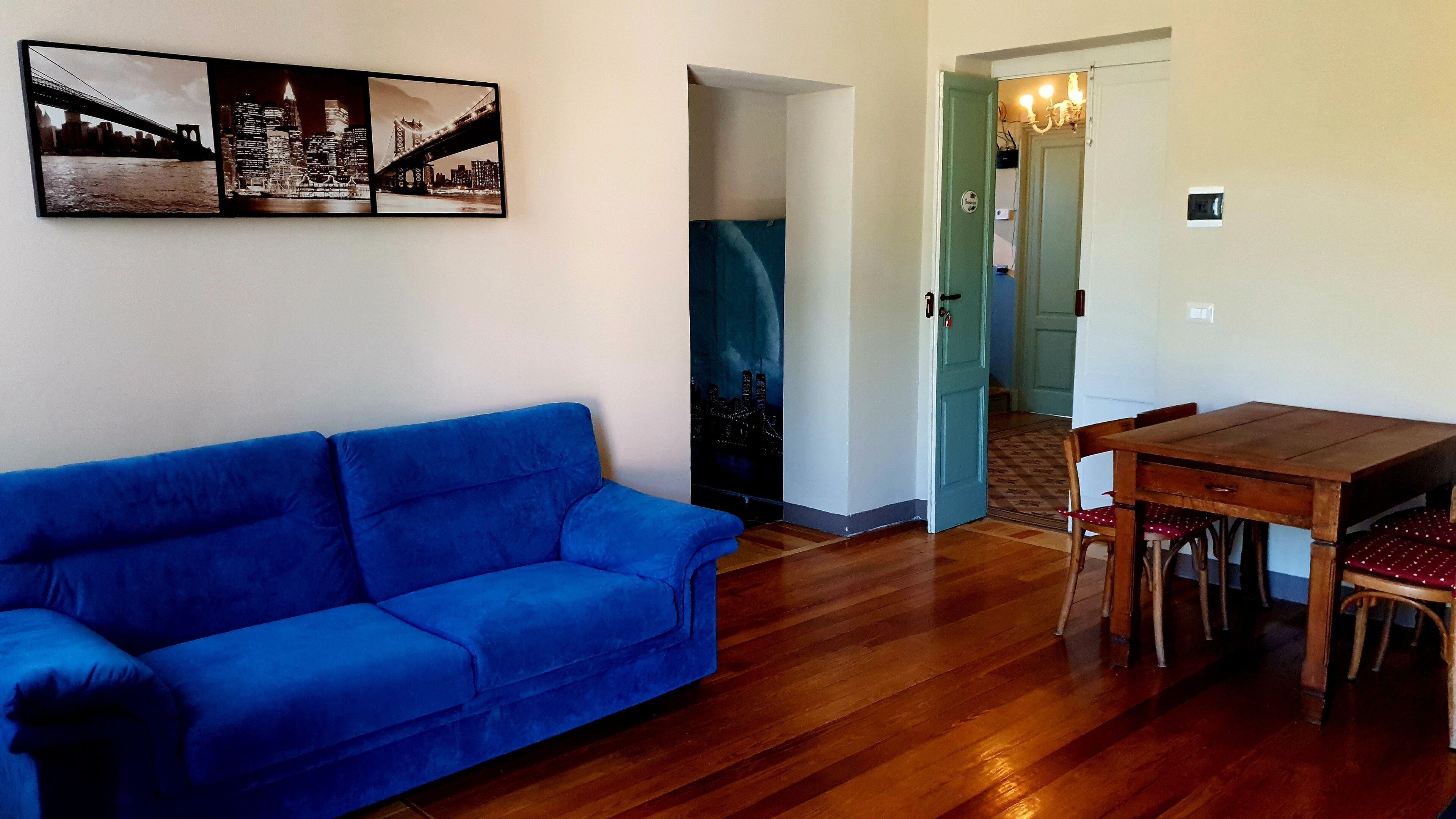 A living room with a blue sofa, a wooden dining table with chairs, and a wall-mounted picture of a bridge.