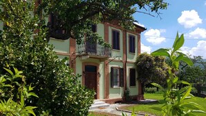 Un bâtiment à deux étages doté d’un balcon, entouré d’une végétation luxuriante et d’une pelouse bien entretenue.