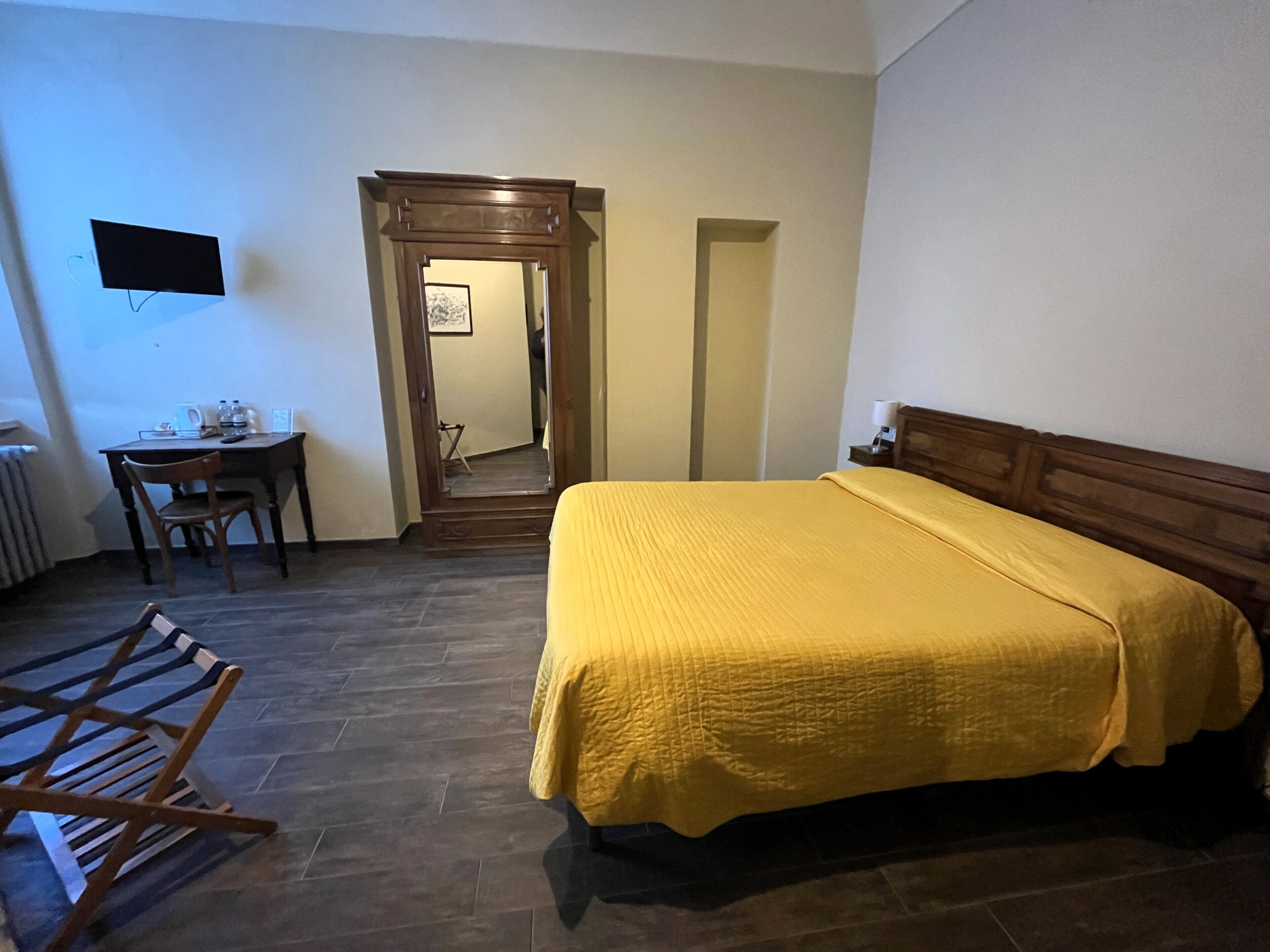 Et hotelværelse med seng, skrivebord, stol, spejl og fjernsyn.
