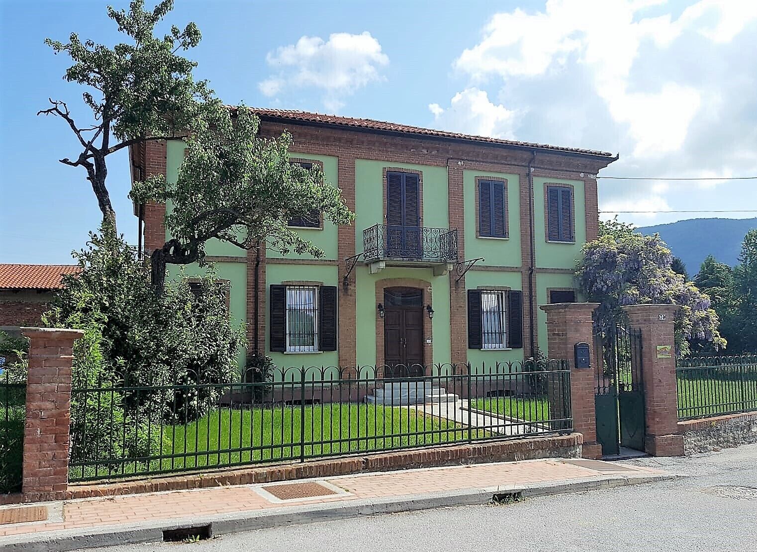 Un edificio de dos plantas con fachada verde, varias ventanas con contraventanas y una entrada con portón.