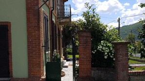 Un bâtiment en briques avec une porte verte, un petit jardin agrémenté de fleurs blanches et un chemin de pierres menant à l’entrée.
