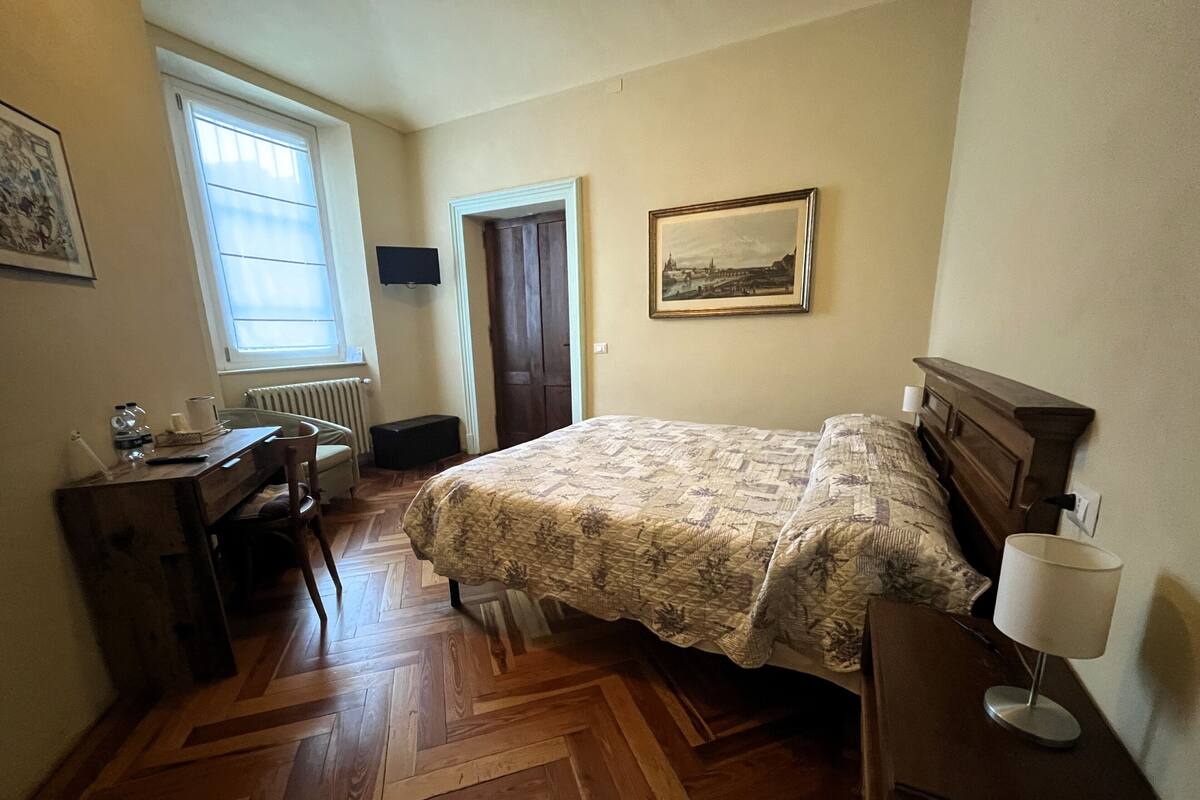 Een slaapkamer met een bed, een bureau, een stoel, een radiator, een raam en een deur.