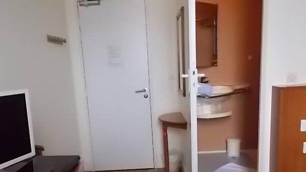 Habitación de hotel con cama, escritorio con computadora, una mesita y baño con lavamanos y espejo.