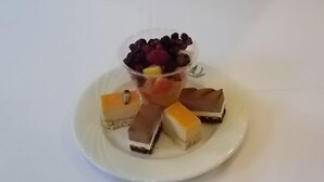 Un plato con diversos postres y una copa de plástico transparente con bayas.
