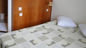 Un dormitorio con cabecera de madera, cama con colcha estampada y almohada blanca.