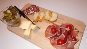 Una tabla de madera con diversos alimentos, como queso, encurtidos, pan en rodajas y embutidos.
