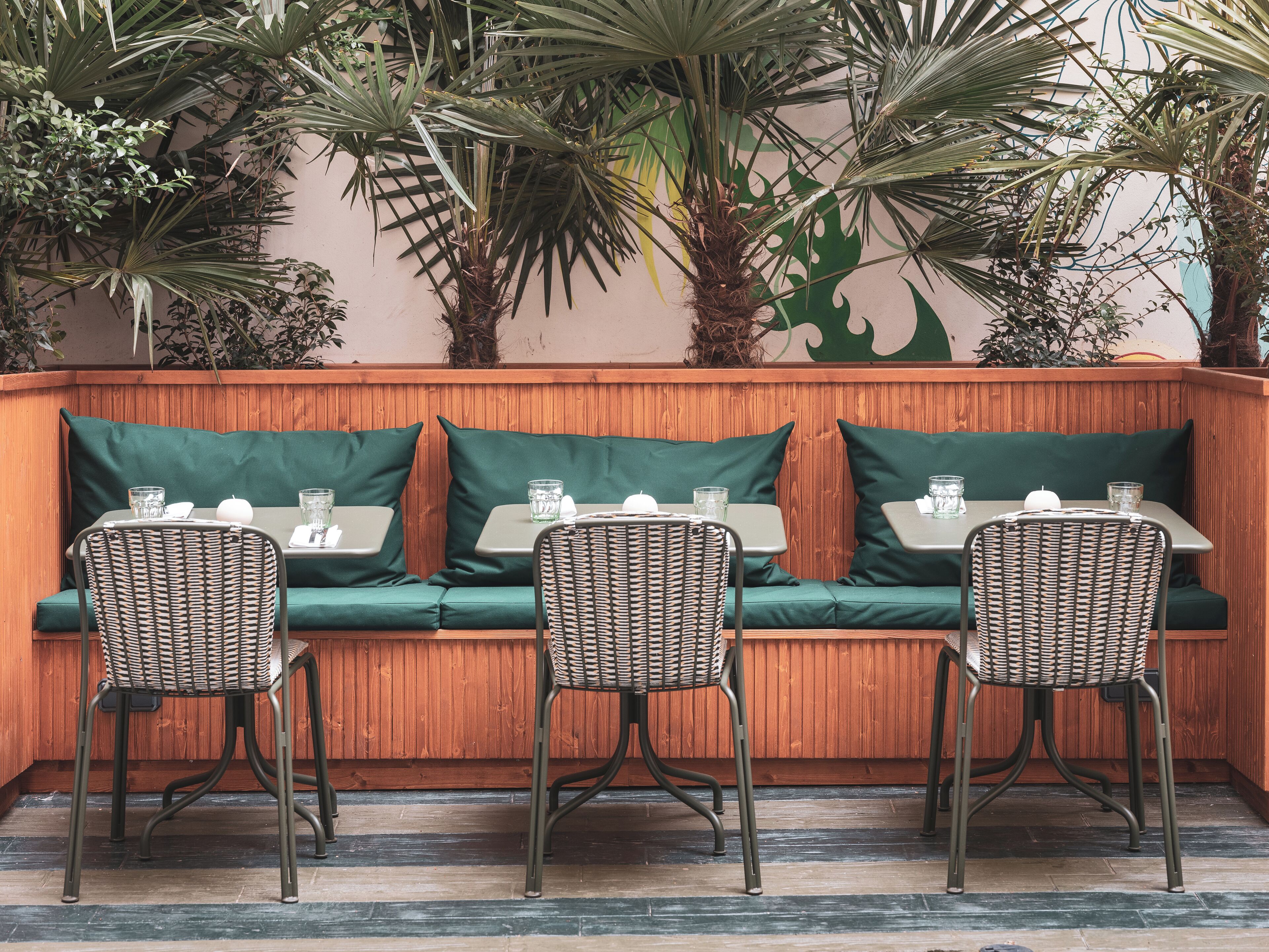 A cozy outdoor seating area with a wooden bench, green cushions, and wicker chairs.