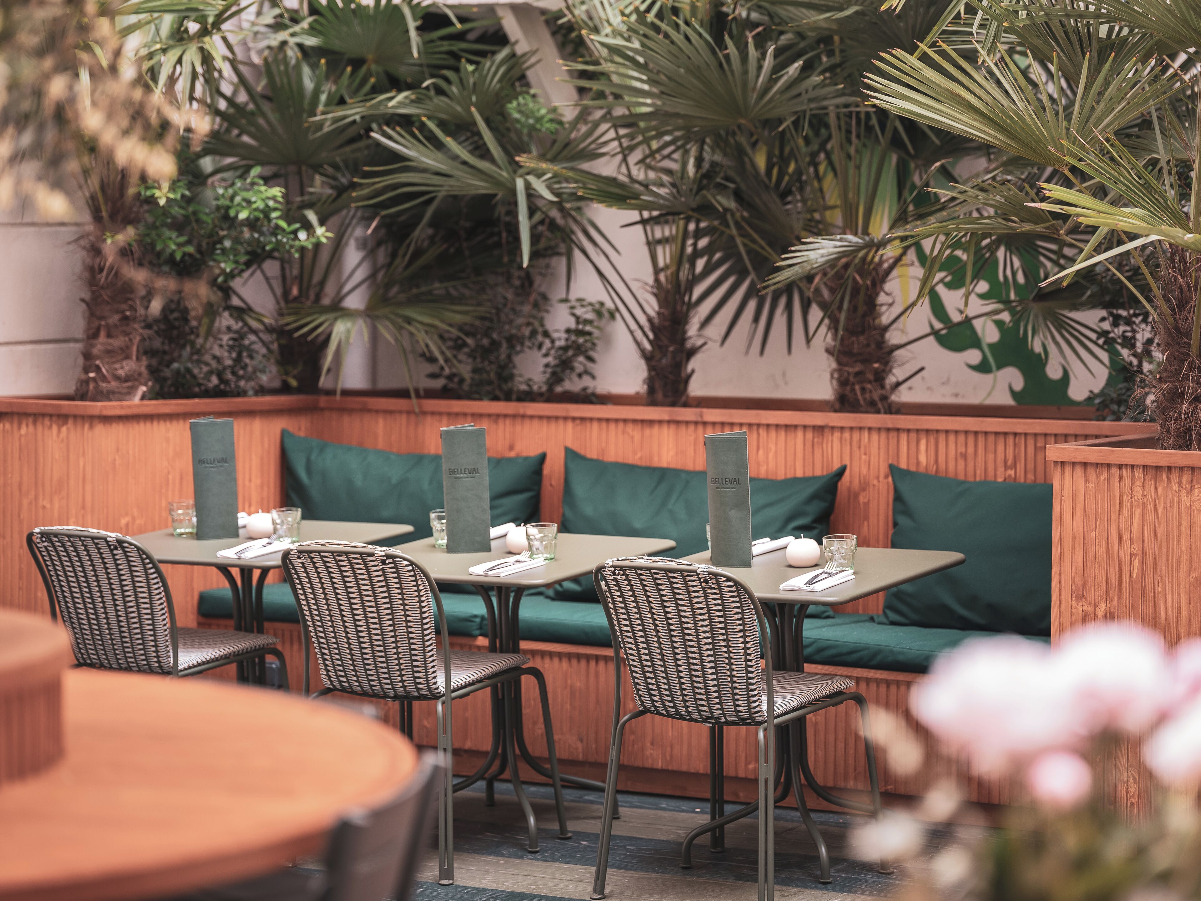 An outdoor seating area with wicker chairs and tables, green cushions, and a wooden bench.