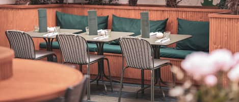 An outdoor seating area with wicker chairs and tables, green cushions, and a wooden bench.