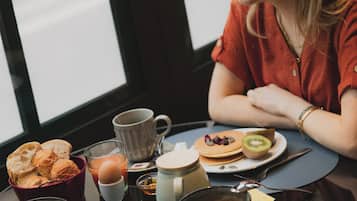 Una escena de desayuno con una mesa, un ventanal y distintos alimentos para el desayuno.