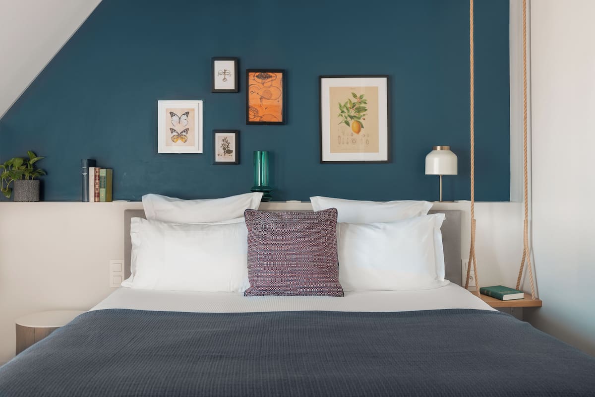 A modern bedroom with a bed, pillows, a hanging plant, and framed artwork on the wall.