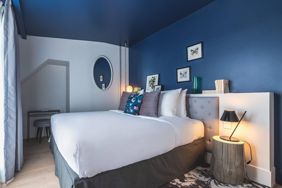 A modern bedroom with a bed, bedside table, lamp, and wall art.