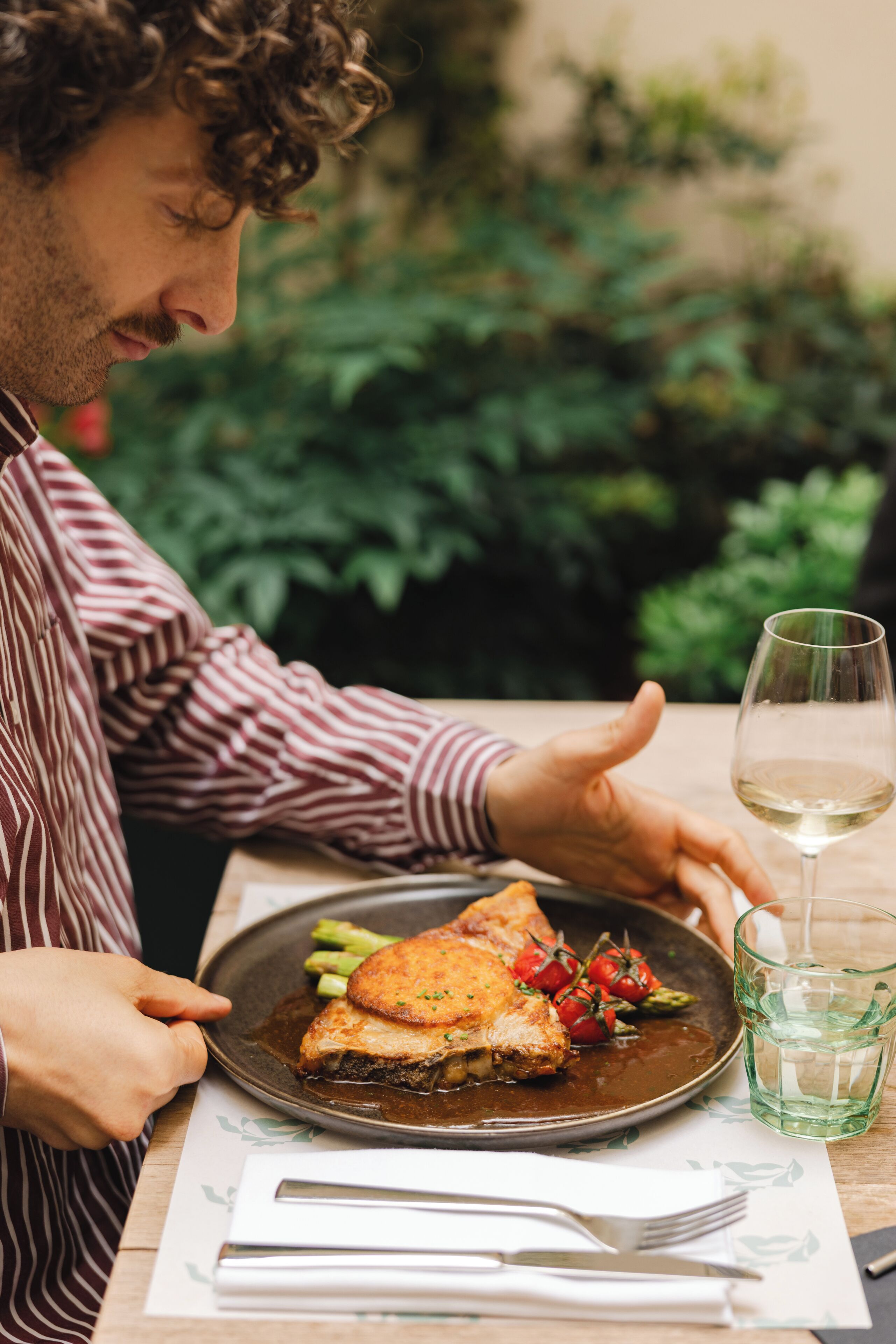 A person dining at an outdoor table with a plate of food, a glass of water, and a fork.