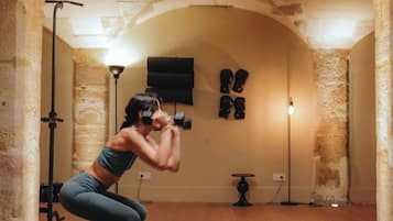 Uma pessoa fazendo um exercício de agachamento em um tapete preto em um quarto com teto abobadado e paredes de pedra.