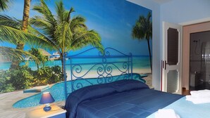 Ein Schlafzimmer mit einem Bett, einem Nachttisch, einer Lampe und einem Wandbild mit Strandmotiv.