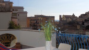 Eine Dachterrasse mit Tisch, Stühlen, einer dekorativen Pflanzvase und Blick auf eine Stadtlandschaft mit Gebäuden und einer Kuppel.