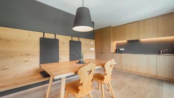 Una cucina moderna con mobili in legno, soffitto scuro e lampada a sospensione sopra un tavolo in legno con due sedie.