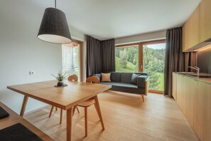 Eine moderne Küche mit Essbereich, einer Couch und Blick auf einen Wald.