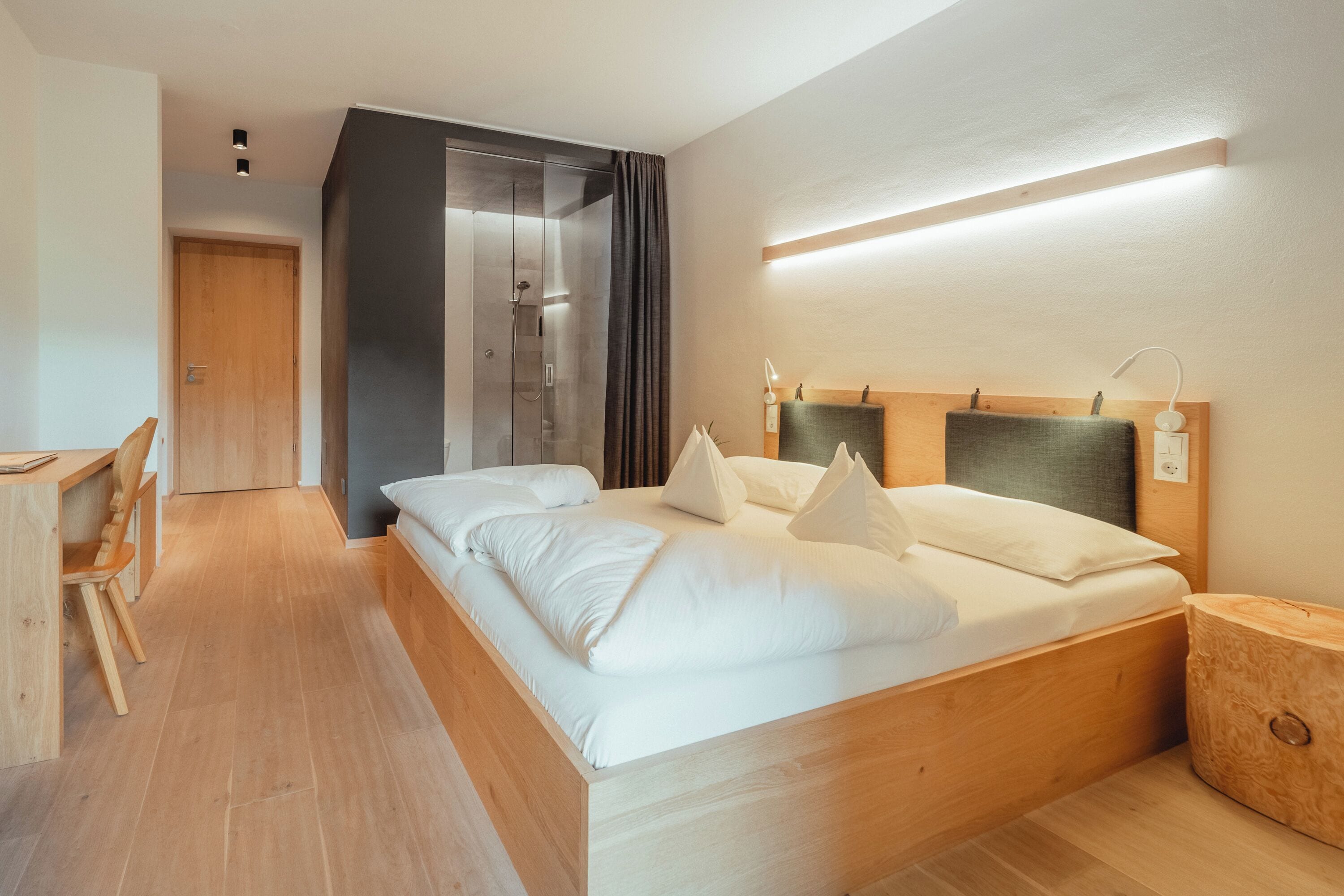 Una camera d'albergo moderna con un letto di legno, una scrivania e un angolo doccia.