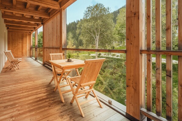 A wooden deck with a table and chairs, overlooking a forested valley.