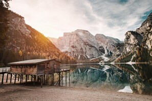Una cabaña de madera sobre pilotes frente a un lago cristalino, con montañas al fondo.