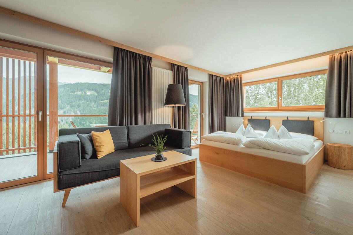 Habitación de hotel moderna con suelo de madera, un sofá, una cama y vistas al exterior.