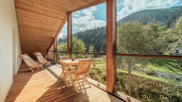 Terraza de madera con mesa y sillas, con vistas a un valle boscoso.